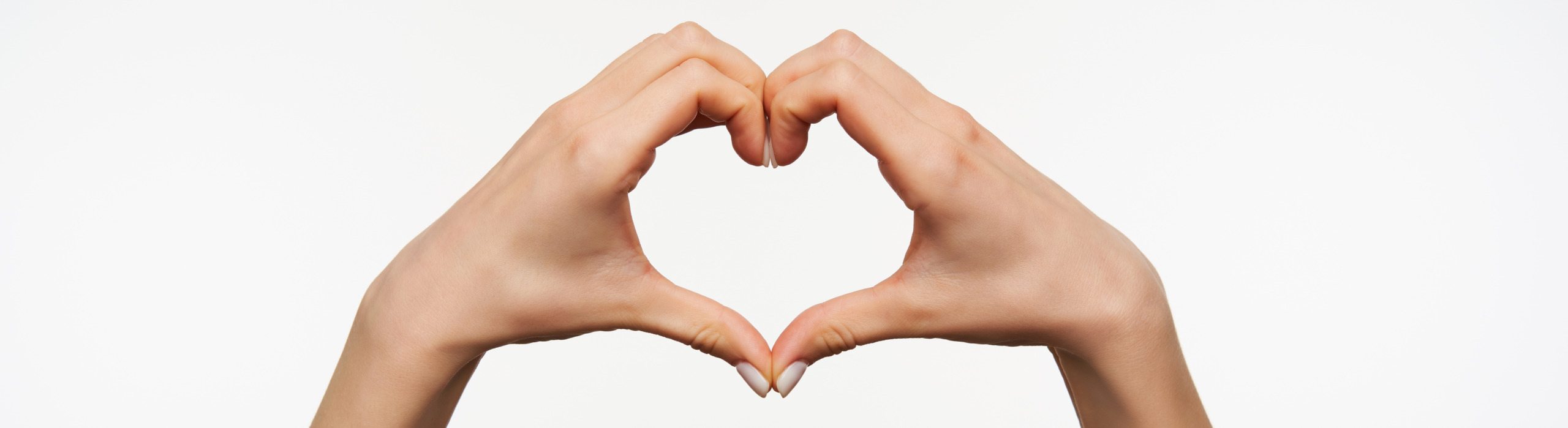 Studio photo of pretty female's hands folding together heart while young woman standing over white background. Language hand symbol viewed from side